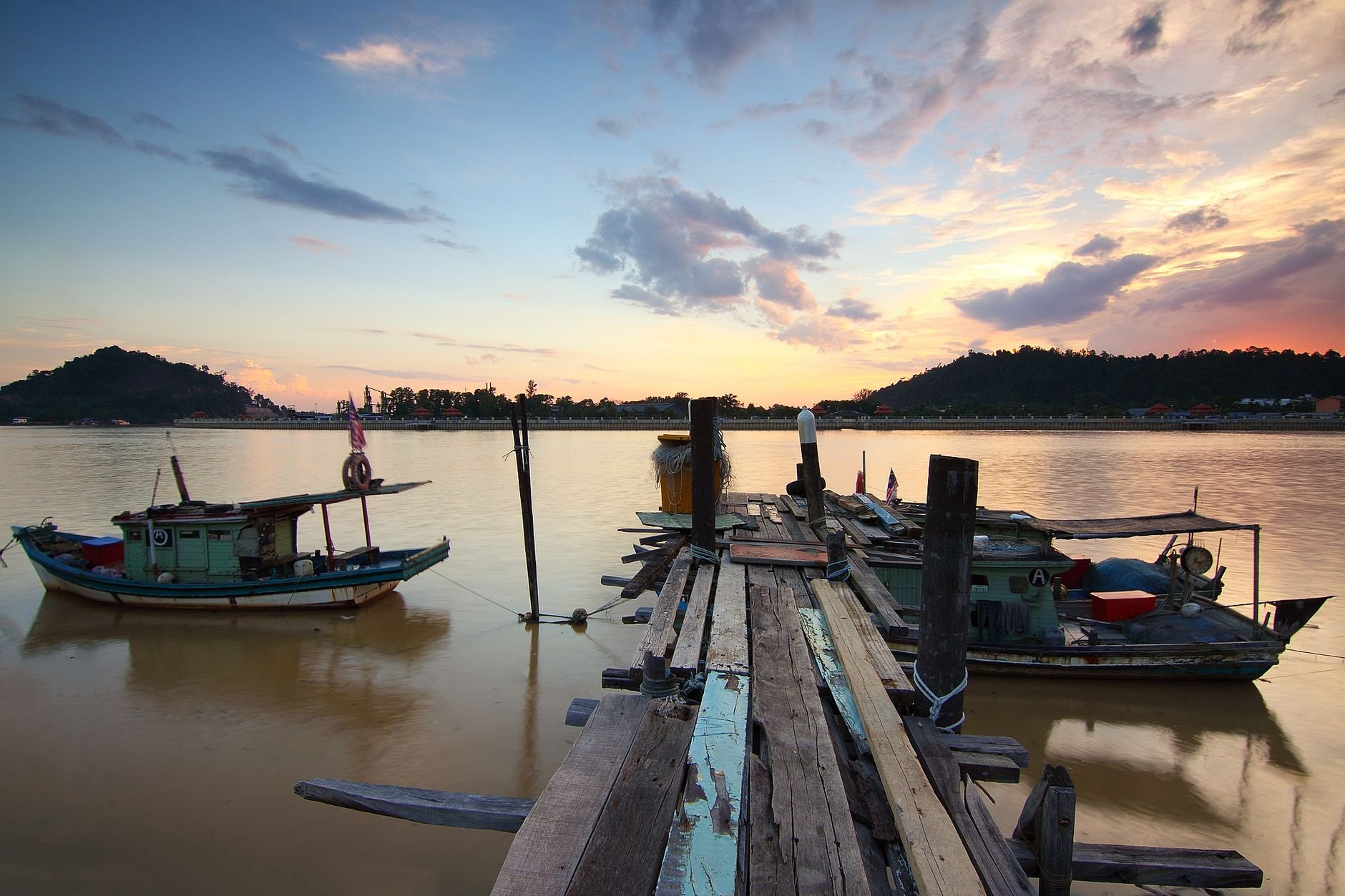 Peaceful scene of wooden dock and fishing boats on tranquil lake during sunset.